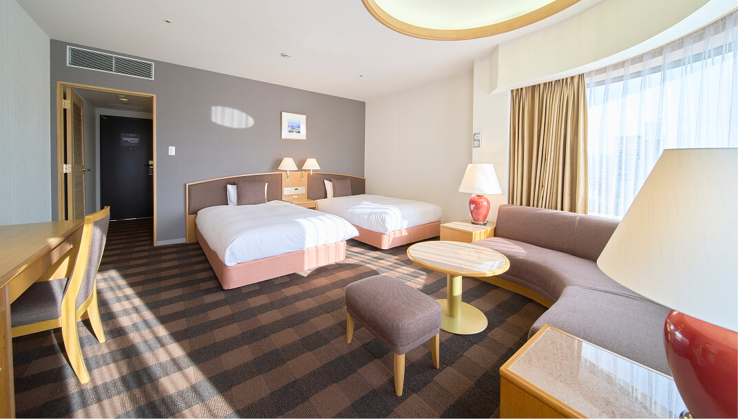 大きな窓とL字型のソファ、テーブルがある開放的なツインルーム