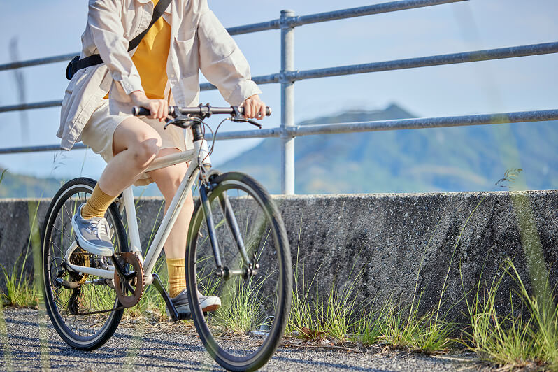 よく晴れた日に、舗装された道路をスポーツタイプの自転車で軽快に走る、リュックを背負った人の姿。